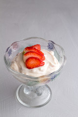 Yoghurt in glass bowl with cut strawberry topping isolated on grey background