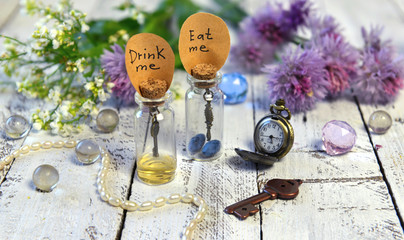 Two cute bottles with tags drink me and eat me, old clocks, key and wild flowers.. Alice in...