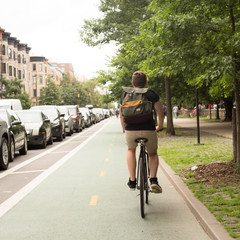 Back view of young hipster caucasian man riding bike on bike lane