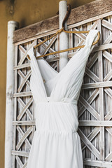 Long white wedding dress hanging outside in traditional bali house on window with white wicker shutters