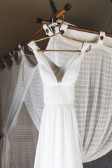 White wedding dress hanging inside room on baldachin with curtains. Bali style
