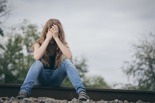 Portrait of young sad ten girl sitting outdoors at the day time.