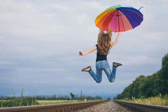 Teen girl with umbrella jumping on the railway at the day time.