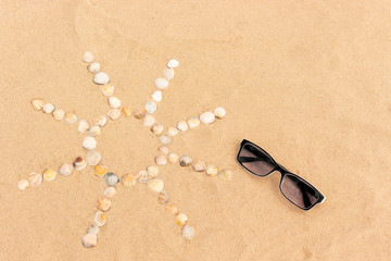 Fototapeta na wymiar abstract sun image made of seashells on a sand with sunglasses
