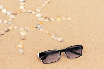 Fototapeta na wymiar abstract sun image made of seashells on a sand with sunglasses