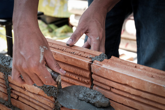 Bricklayer worker installing brick masonry on exterior wall.