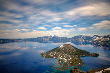 Long exposure of a deep blue lake with an island in the middle and reflections on the water