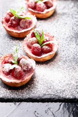 Homemade strawberries tarts with powdered sugar on slate plate, black background. Close up.