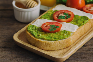 Open sandwich for breakfast or lunch. Sandwich spread with cream cheese,  avocado and tomato.Avocado and cream cheese open sandwich style serve with orange juice on rustic wood table in close up view.