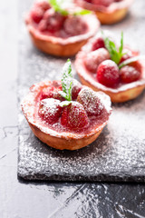 Homemade strawberries tarts with powdered sugar on slate plate, black background. Close up.