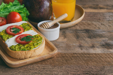 Open sandwich for breakfast or lunch. Sandwich spread with cream cheese,  avocado and tomato. Avocado and cream cheese open sandwich style serve with orange juice on rustic wood table with copy space.