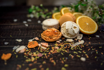 Obraz na płótnie Canvas Multicolor macaroons of white and orange color with sliced orange fruits on a wood background with some crushed candy and blossom cherry