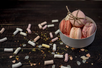 Multi color pastel macaroons in white deep plate decorated with rope on a black wood background