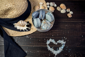 Straw hat with blue macaroons and sea salt with shells on the wood background