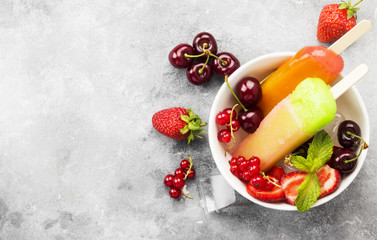Multi-colored popsicles with strawberry, red currant and cherry on a gray background. Top view, copy space. Food background