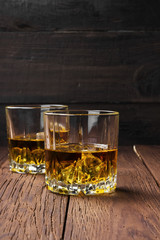 Whisky with ice in two glasses on a wooden background