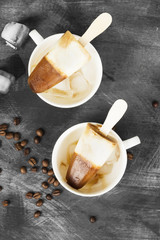 Coffee ice cream popsicles in white cups on a dark background. Top view. Food background