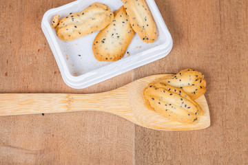 Home made a small sweet cookie with black sesame, typically round, flat, and crisp.Cookie in dish on wood spoon.