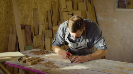 20s bearded carpenter drawing in workshop in sunny day