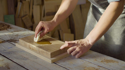 Portrait of 20s bearded carpenter woodworker rubs lacquer in a wooden plank in the workshop