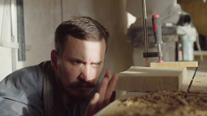 20s bearded woodworker using brashing machine tool and checking quality of work