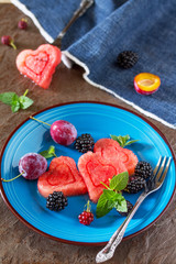 Various fresh fruits and berries on a plate on a brown stone or slate background - watermelon, blackberries, plums and grapes.