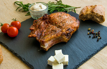 Fried pork rib on a stone plate with tomatoes, herbs and cheese.