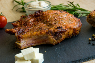Fried pork rib on a stone plate with tomatoes, herbs and cheese.