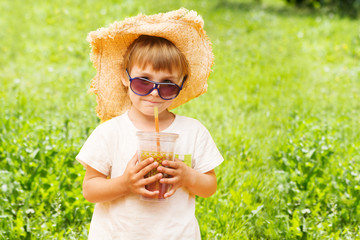 Little funny boy drinking a fresh juice through a straw on  summer background  .