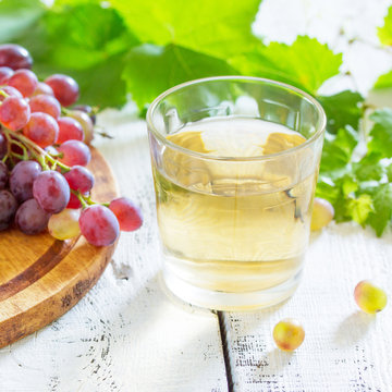 A glass of sweet grape juice, freshly squeezed, a bunch of fresh grapes on a white wooden table.