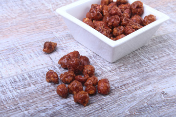 Sugared Hazelnuts in a white bowl on a wooden background. Hazelnuts in sugar glaze. Selective focus.