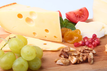 Assortment of cheese with fruits, grapes, nuts and cheese knife on a wooden serving tray.