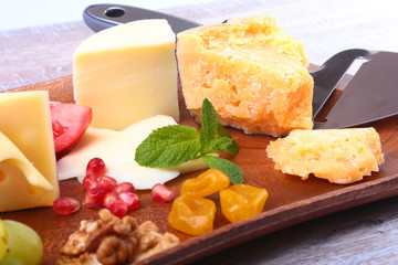 Assortment of cheese with fruits, grapes, nuts and cheese knife on a wooden serving tray.
