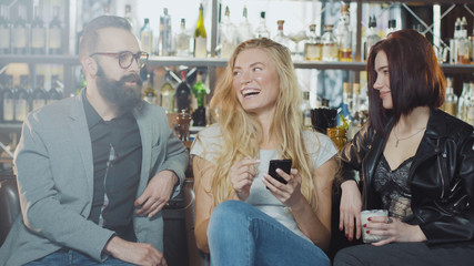 3 person company of friends are taking selfie behind bar counter, smiling and looking at smartphone camera with happy emotions faces