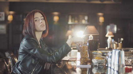 20s sexy beauty redhead woman in black leather jacket is drink cocktail, looking at camera and...