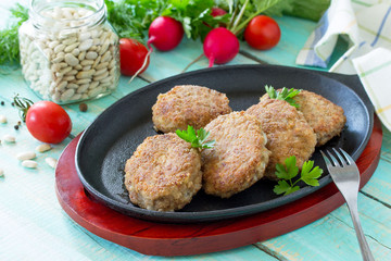 Homemade meatballs with white beans and fresh herbs. Cast-iron frying pan full of delicious fried meat cutlets, fresh greens and vegetables on the kitchen table.