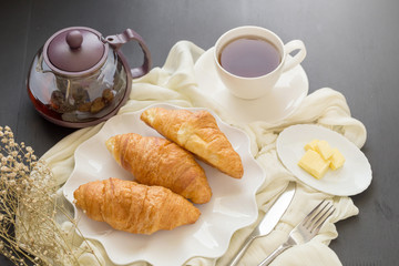 Freshly baked croissants and cup of tea on a white plate on a dark table background. in a windows light. Breakfast concept