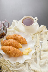 Freshly baked croissants and cup of tea on a white plate on a dark table background. in a windows light. Breakfast concept