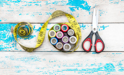 Сolored threads wrapped by the measuring tape with scissors on a wooden background. Top view.