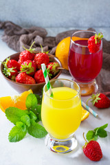 Refreshing summer drinks assortment. Orange juice, strawberry juice, fresh oranges and strawberries on a gray stone or slate background.