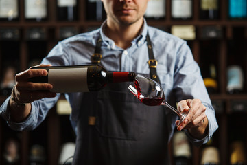Male sommelier pouring red wine into long-stemmed wineglasses. - obrazy, fototapety, plakaty