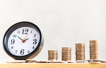 Alarm clock and step of coins stacks on the table with loft style background, money, saving and investment or family planning concept.