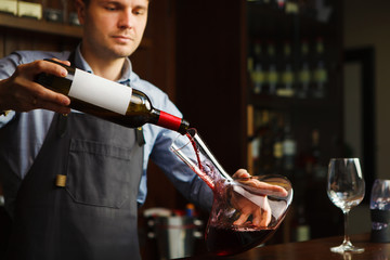 Sommelier pouring wine into glass from decanter. Male waiter