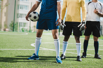 partial view of soccer players and referee standing on soccer pitch before game