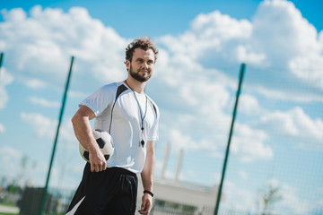 portrait of referee holding soccer ball while standing on soccer pitch