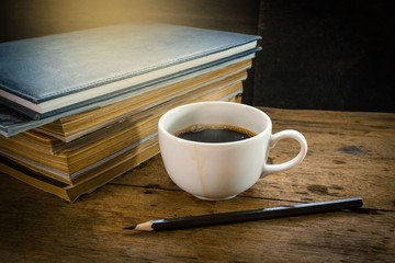 White cup of hot coffee with stack old book on rustic wood table.Relaxing time with coffee in the morning.