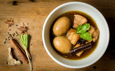Eggs and pork in brown sauce frogs with spice and herbs on wooden table. Thai food on top view.