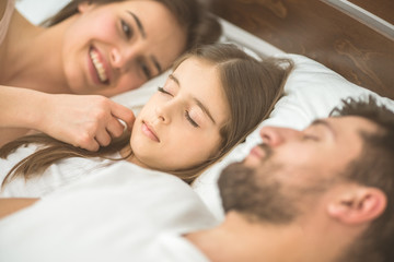 Obraz na płótnie Canvas The little girl sleeping near the parents in the bed