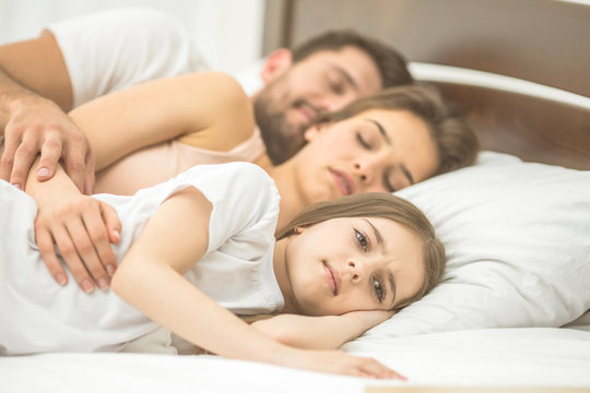 The daughter lay near the sleeping parents on the bed