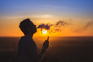 The man smoke electronic cigarette on the sunset backround
